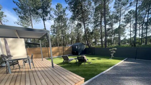 A wooden deck with a covered seating area, a grassy lawn, and a small shed in a wooded area.