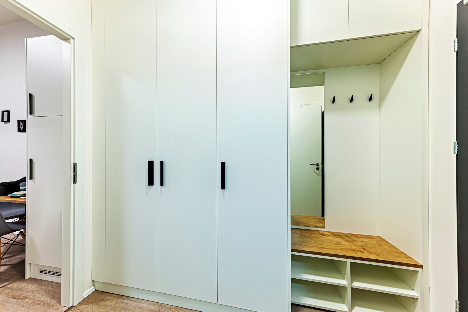 A room with a large white wardrobe, a wooden bench, and a mirror.