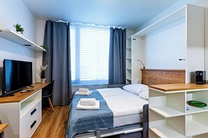 A modern hotel room with a bed, a desk with a TV, a computer, and a window with curtains. - MamaStay Andel apartments (Prague)
