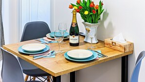 A dining table set with plates, cutlery, a bottle of champagne, and a vase of tulips. - MamaStay Andel apartments (Prague)