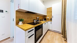 A modern kitchen with white cabinets, a wooden countertop, a built-in oven, and a coffee maker. - MamaStay Andel apartments (Prague)
