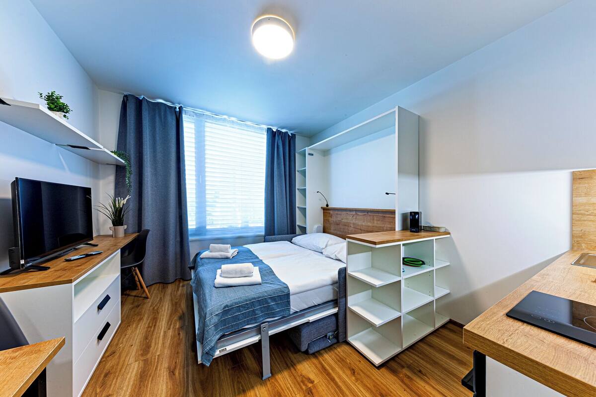 A modern hotel room with a bed, a TV, a desk, and a large window with curtains.