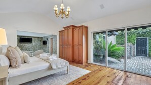 A bedroom with a bed, wooden wardrobe, and a large sliding glass door leading to a garden. - Luxury Living w/ Private Pool + Parking Steps to River by Lucky Savannah (Savannah)