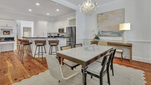 A modern kitchen with white cabinetry, a stainless steel refrigerator, and a dining area with a marble table and bar stools. - Luxury Living w/ Private Pool + Parking Steps to River by Lucky Savannah (Savannah)