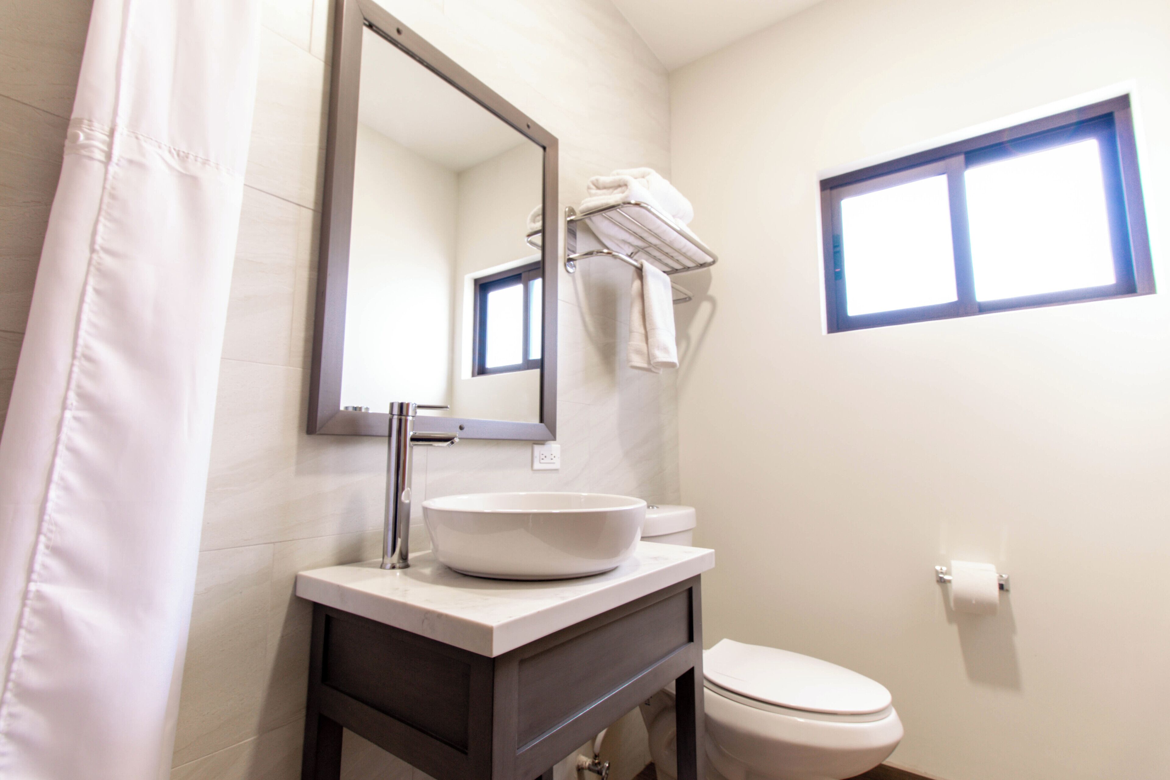 A bathroom with a white sink, a mirror, a towel rack, a toilet, and a window.
