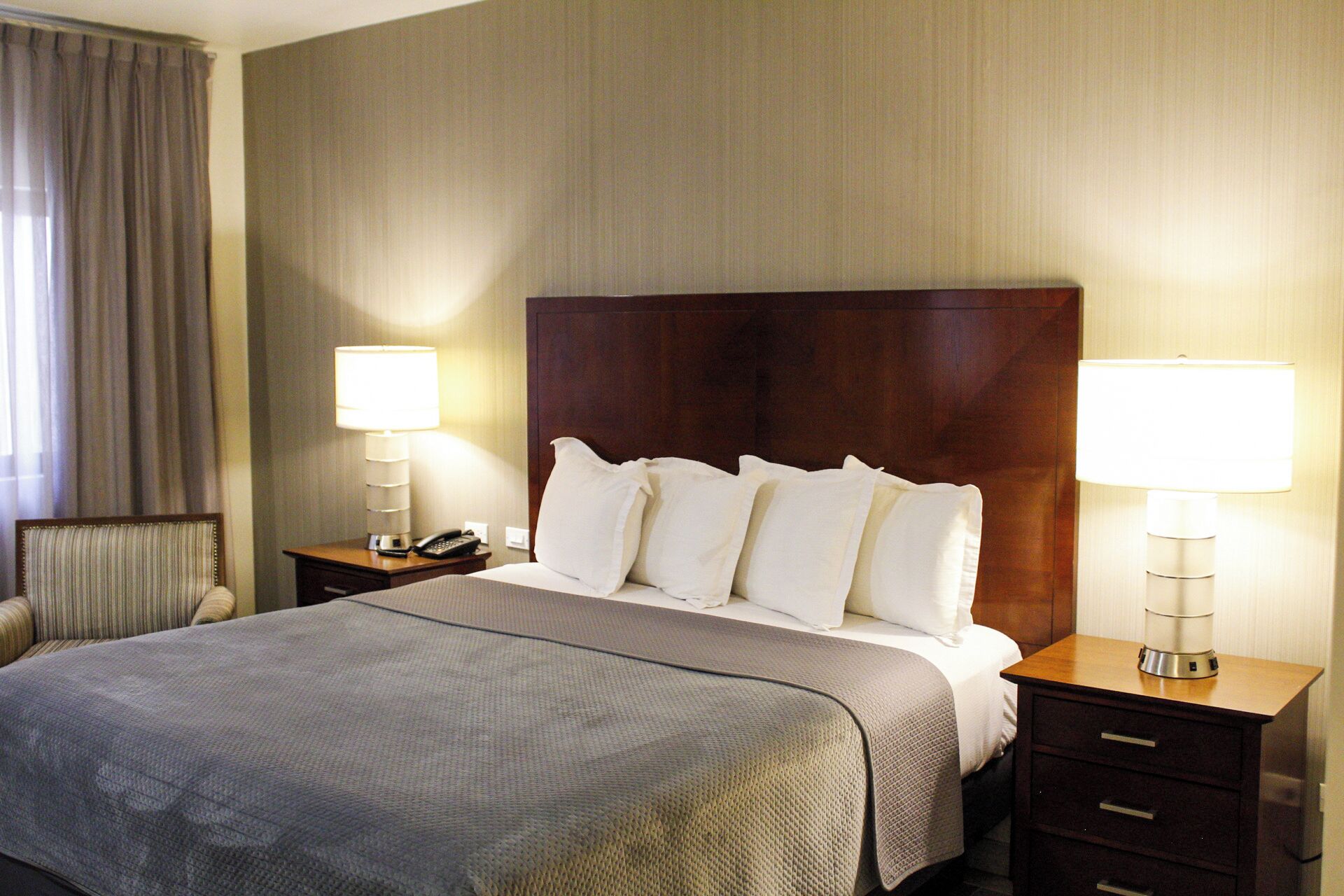 A hotel room with a large bed, two bedside tables, a telephone, and two lamps.