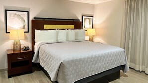 A hotel room with a large bed, two bedside tables with lamps, a wooden headboard, and a framed picture on the wall.