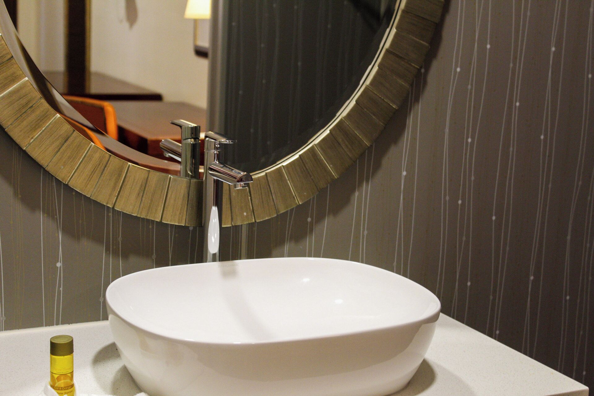A bathroom with a white sink, a round mirror with a gold frame, and a bottle of lotion on the counter.