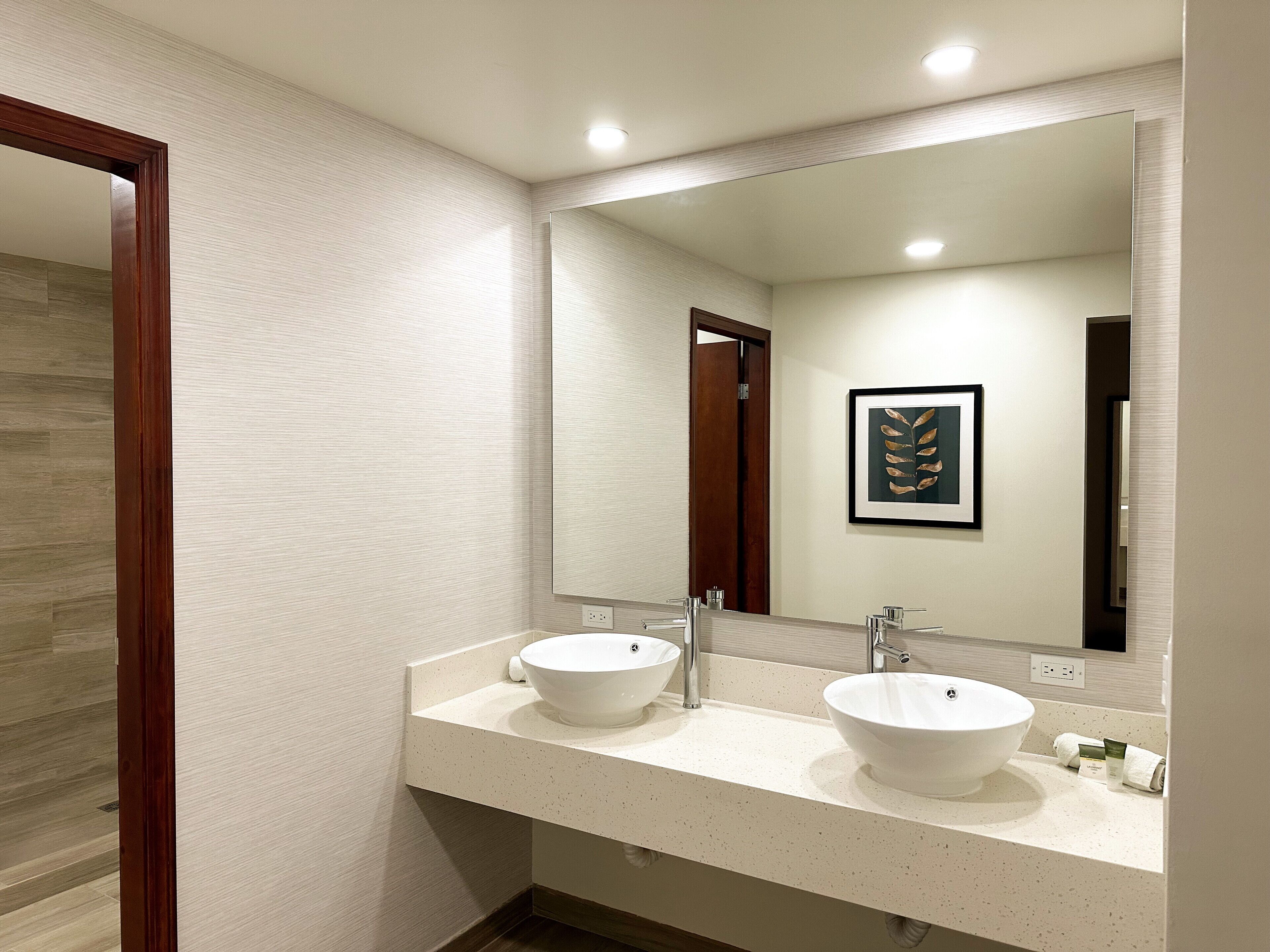 A modern bathroom with two sinks, a large mirror, and a framed artwork on the wall.
