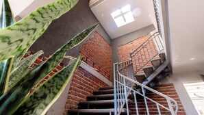 A staircase with a metal railing, a brick wall, and a large window with a cross symbol.