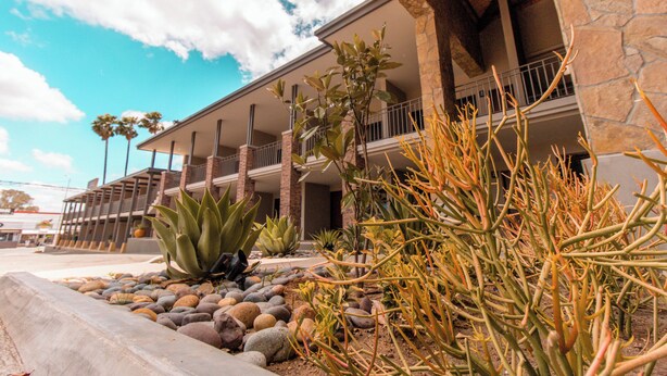 A hotel with a stone facade, multiple balconies, and a landscaped garden with various plants and rocks.