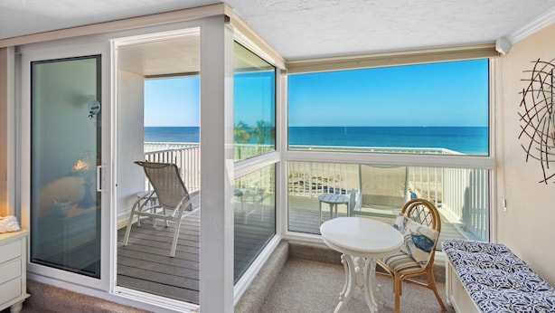 A sunlit room with a view of the ocean, a sliding glass door, a white table, and a bench. - Luxury on the Sand – Large Oceanfront Condo La Playa #202D by RVA (Longboat Key)