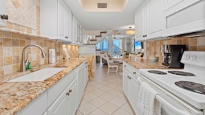 A modern kitchen with white cabinets, a granite countertop, a stove, and a view of the living area. - Luxury on the Sand – Large Oceanfront Condo La Playa #202D by RVA (Longboat Key)