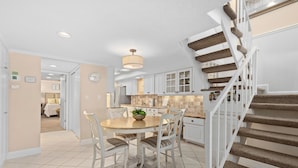 A kitchen with white cabinets, a dining table with chairs, a staircase with carpeted steps, and a hanging light fixture. - Luxury on the Sand – Large Oceanfront Condo La Playa #202D by RVA (Longboat Key)