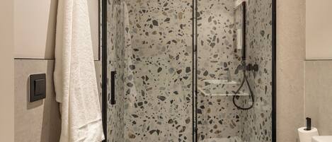 A modern bathroom with a glass-enclosed shower, a white toilet, and a towel hanging on a rack.