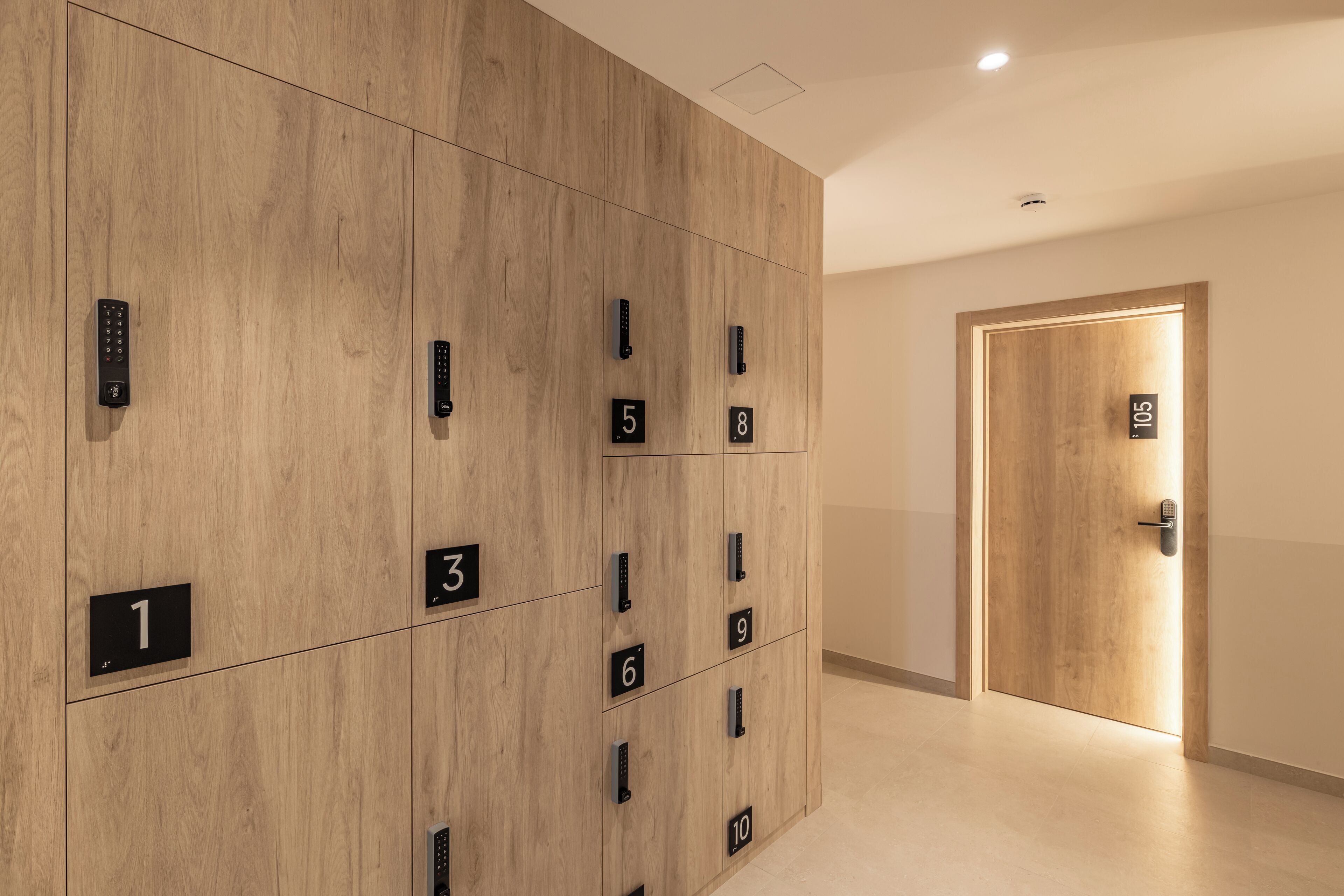 A modern hotel lobby with a wooden panel wall displaying numbered lockers and a door labeled 105.