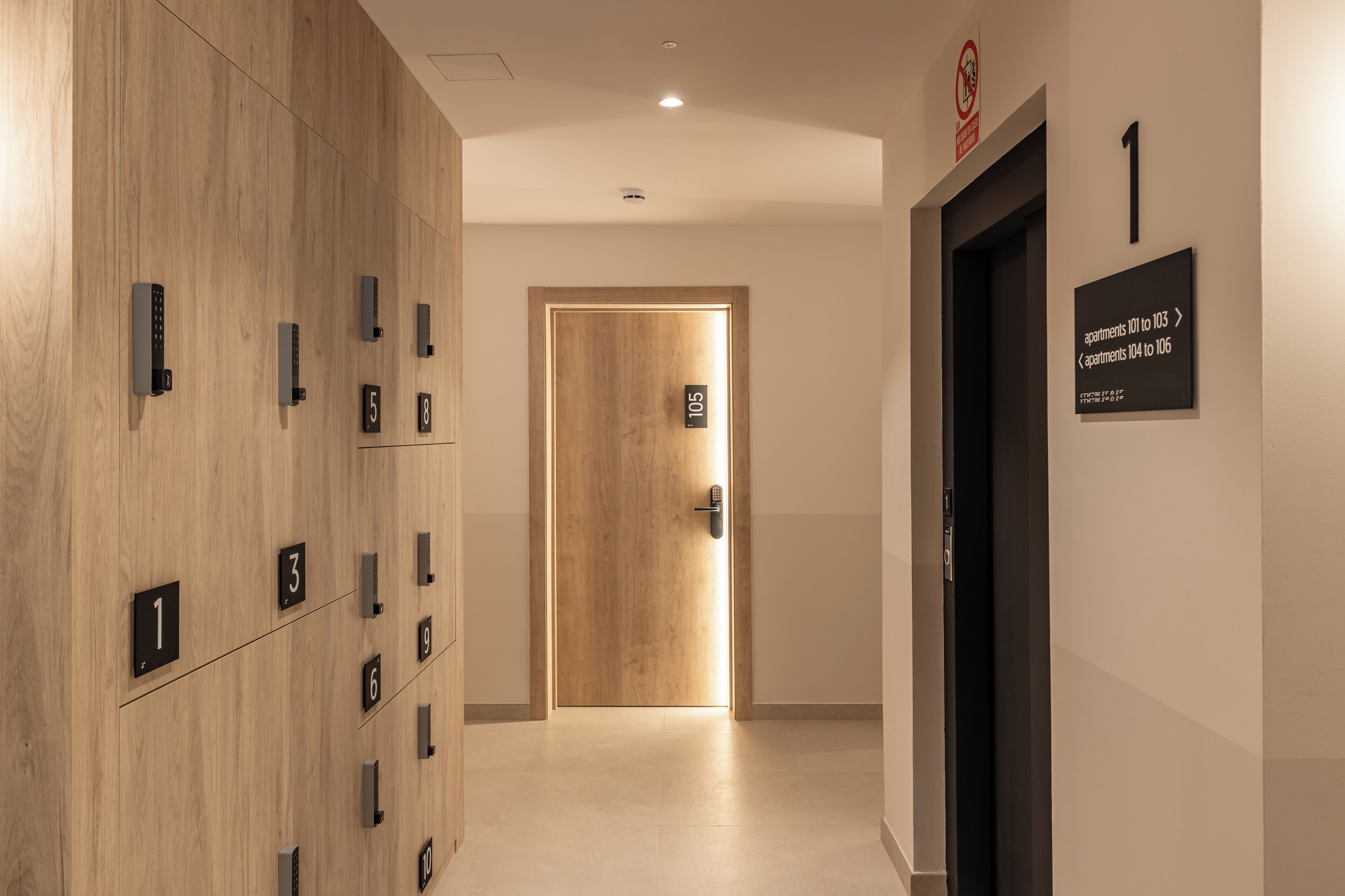 A hallway with numbered doors leading to apartments, a wooden wall with door numbers, and a sign indicating apartment numbers 101 to 106.