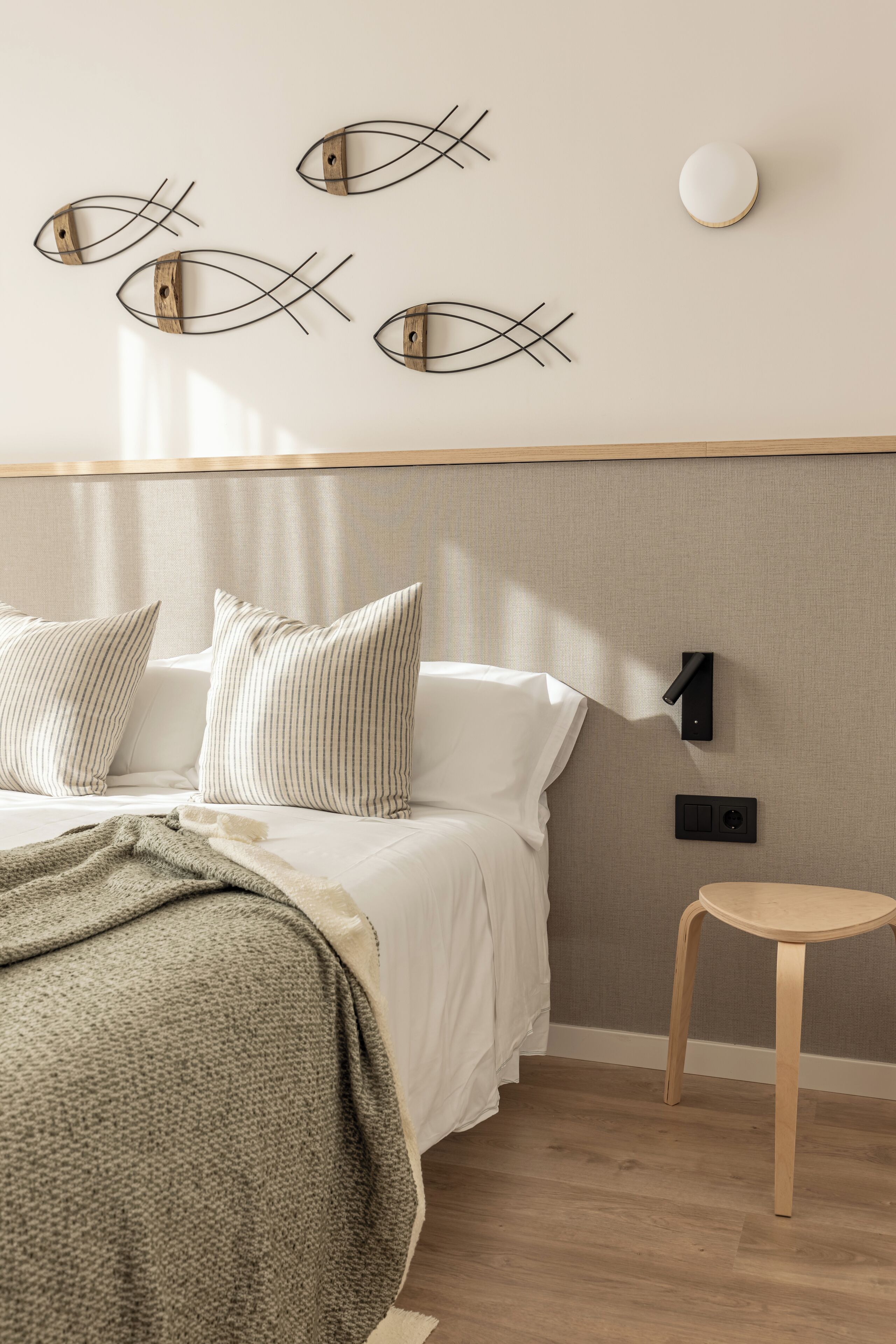 Een slaapkamer met een bed, kussens, een nachtkastje, een wandlamp en een kunstwerk aan de muur.
