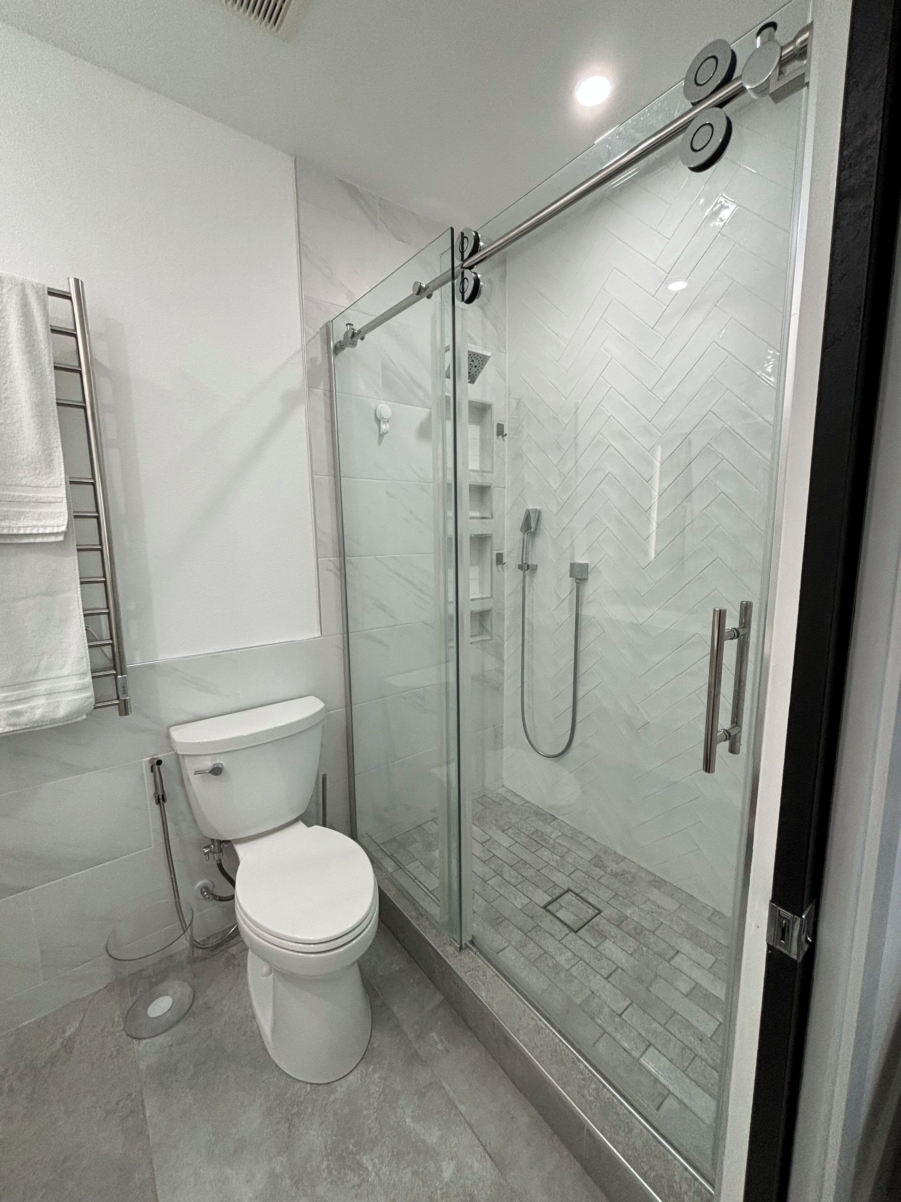 A modern bathroom with a glass-enclosed shower, a toilet, and a towel rack.