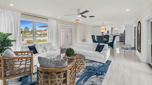 A spacious living room with a white sofa set, a wooden coffee table, and a large window offering a view of the outdoors. - Stunning 4 Bed I Heated Pool/Hot Tub (Marco Island)