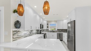 A modern kitchen with white cabinetry, a marble island, and a stainless steel refrigerator. - Stunning 4 Bed I Heated Pool/Hot Tub (Marco Island)