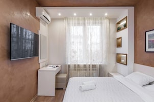 Un dormitorio moderno con una cama, un escritorio, un tocador y un ventanal con cortinas traslúcidas.
