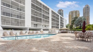 A modern hotel with a pool area, lounge chairs, and a view of tall buildings. - Charming 2-bedroom condo nearby the beach with WiFi, AC in Sunny Isles Beach (Sunny Isles Beach)