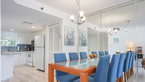 A modern kitchen with white appliances, a dining area with a glass table and blue chairs, and a large mirror reflecting the space. - Charming 2-bedroom condo nearby the beach with WiFi, AC in Sunny Isles Beach (Sunny Isles Beach)