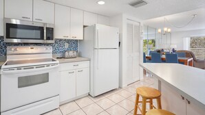 A modern kitchen with white cabinetry, a stainless steel microwave, a built-in oven, a toaster, and a refrigerator. There is a dining area with a table and chairs visible through a glass door. - Charming 2-bedroom condo nearby the beach with WiFi, AC in Sunny Isles Beach (Sunny Isles Beach)