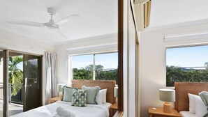 Ein Hotelzimmer mit Bett, Nachttisch, Deckenventilator und Blick auf Bäume durch das Fenster.