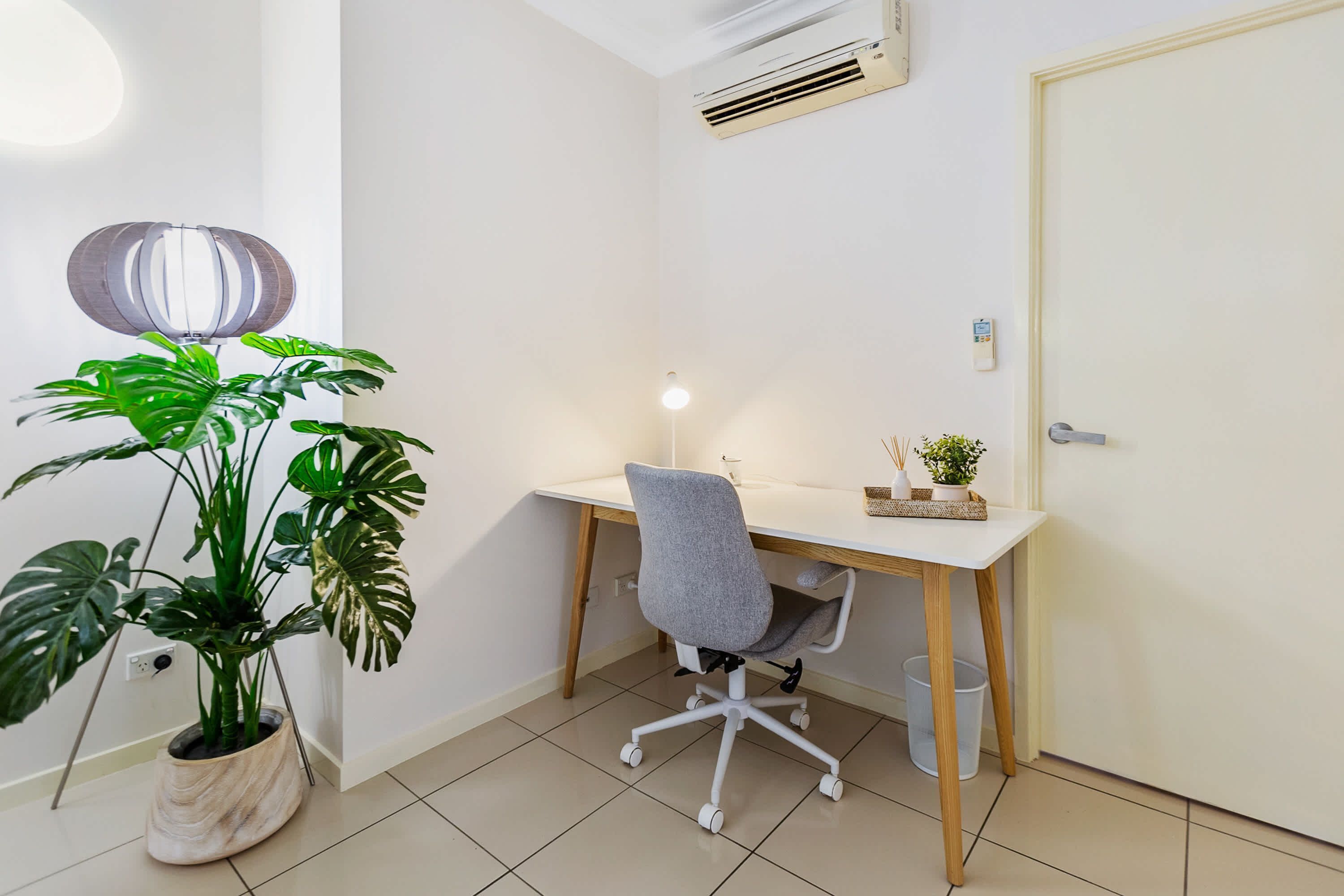A small, clean office space with a desk, chair, potted plant, and a wall-mounted air conditioner.