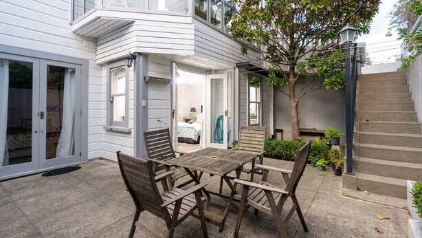 A patio with a wooden table and chairs, a small tree, and a staircase leading to a second floor. - A Historic Wellington Escape (Wellington)
