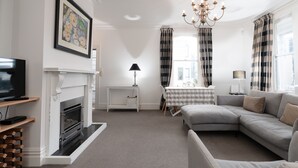 A living room with a fireplace, a sofa, a television, and a dining table with chairs. - A Historic Wellington Escape (Wellington)