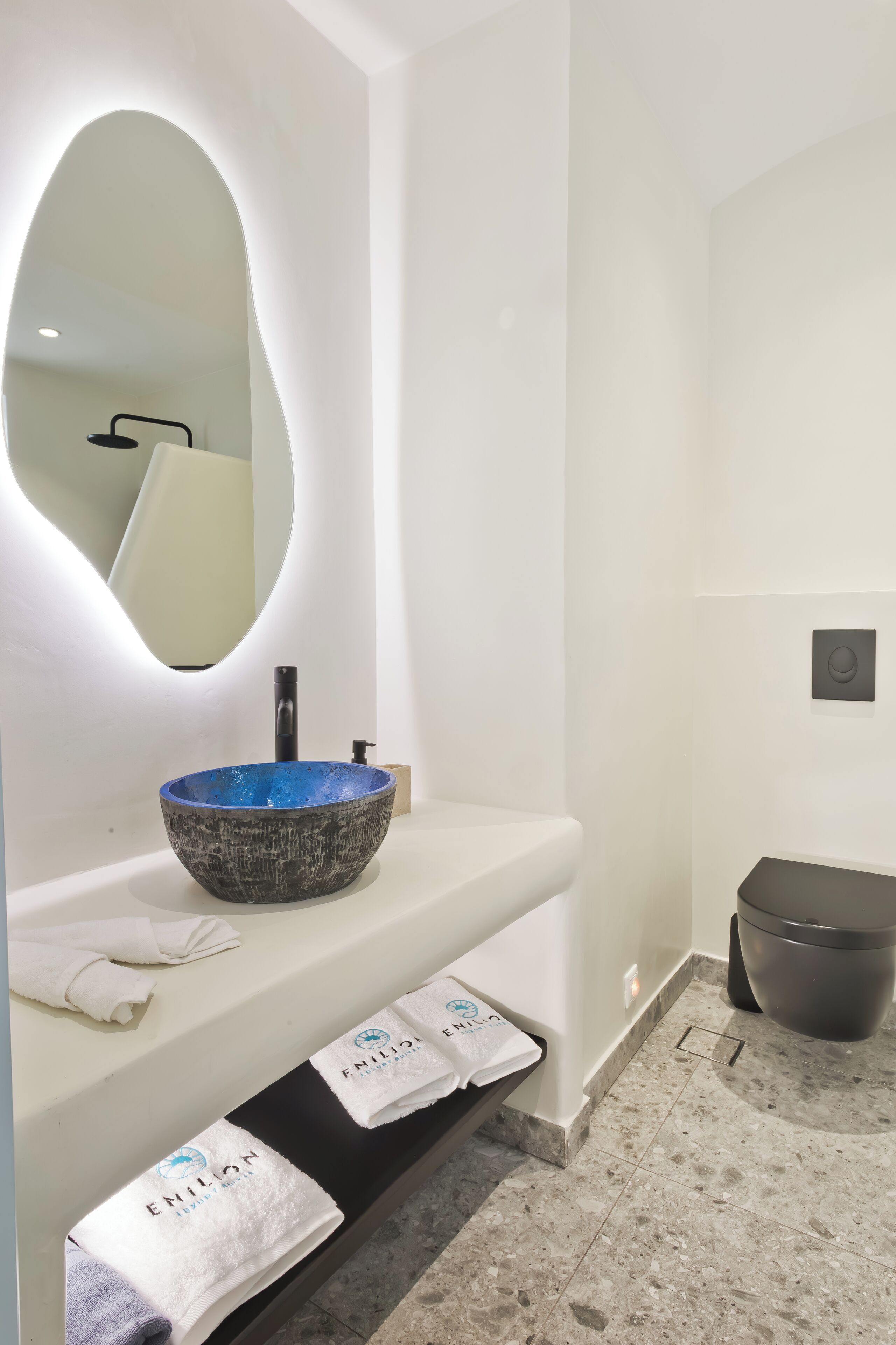 Ein modernes Badezimmer mit einem weißen Waschtisch, einem blauen Keramikbecken, einem großen Spiegel und einer schwarzen Toilette.