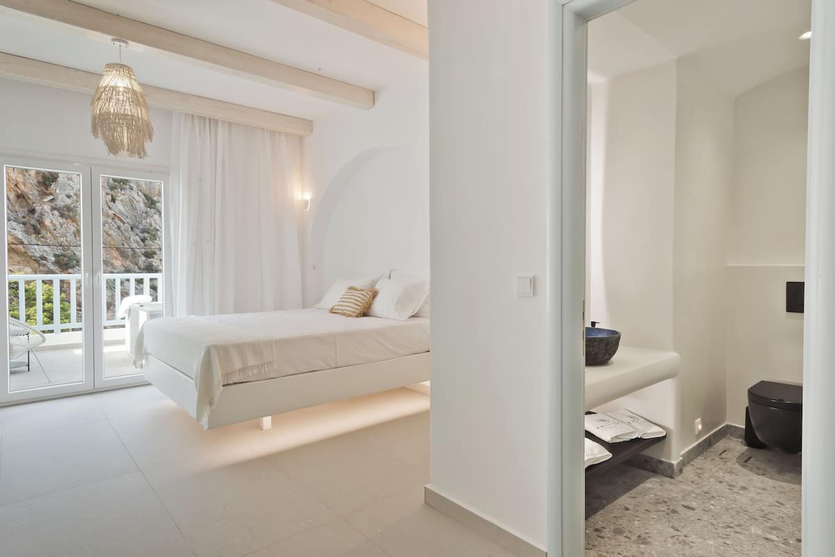 A modern bedroom with a bed, a bathroom with a toilet and sink, and a balcony with a chair.