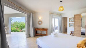 Ein Schlafzimmer mit einem großen Bett, einem Nachttisch aus Holz, einem Spiegel und Blick ins Grüne.