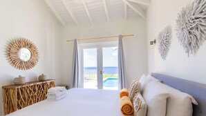 Ein Schlafzimmer mit Bett, einem Holzkonsolentisch, Blick auf das Meer und Wanddekoration.