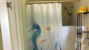 Un baño con cortina de ducha con escena submarina, un perchero con toallas y un cabezal de ducha.