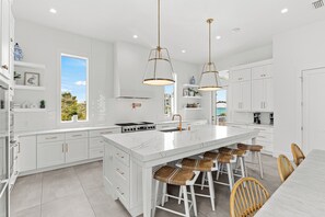 A modern kitchen with white cabinetry, a large island with stools, pendant lighting, and a view of the outdoors.