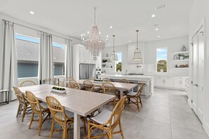 A modern kitchen with white cabinetry, a large island, and a dining area with wicker chairs.