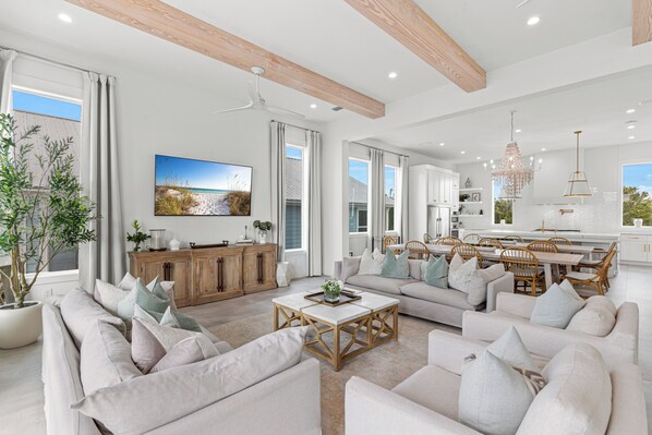 A spacious living area with a large sofa set, a dining table with chairs, and a kitchen area with white cabinetry.