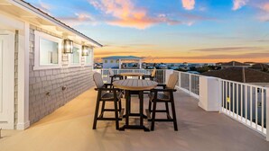 Un balcon avec une table et des chaises, une balustrade blanche et une vue sur des maisons au loin.