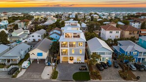Un quartier résidentiel en bord de mer, avec des maisons, une piscine et une vue sur l’océan au coucher du soleil.