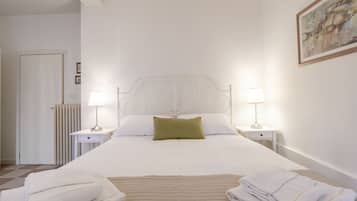 A neatly made bed with white linens and a green pillow, flanked by two bedside tables with lamps.