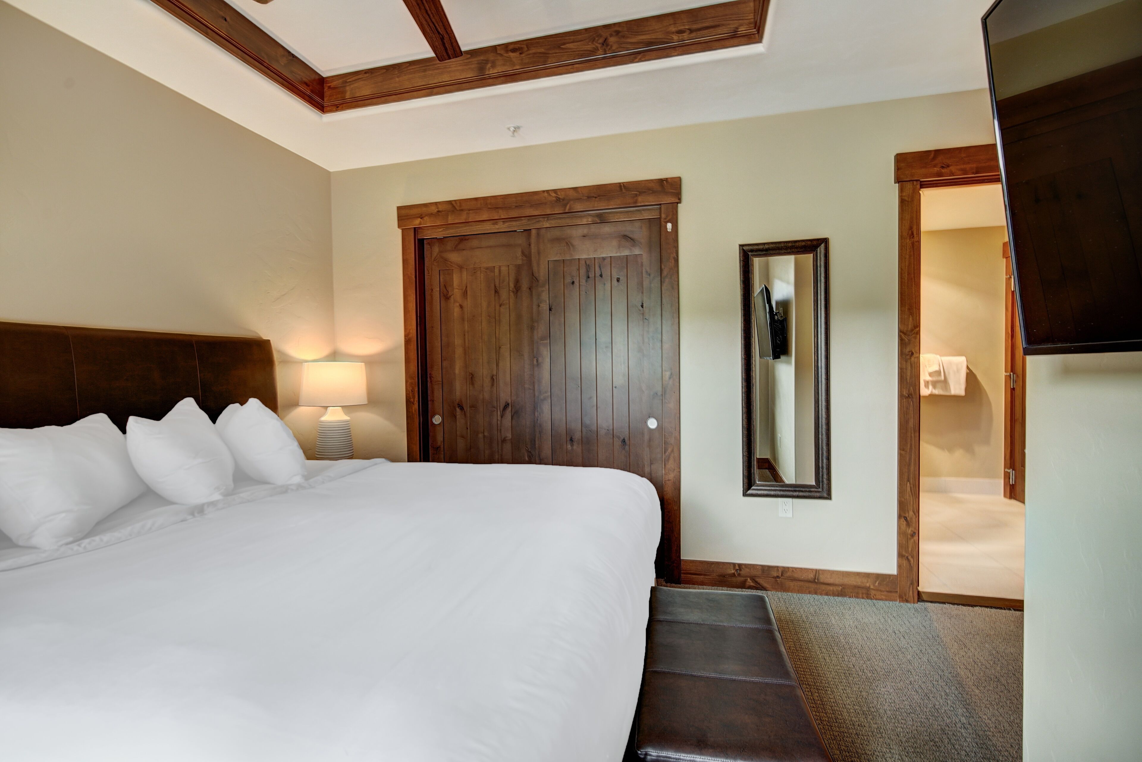 A bedroom with a large bed, a wooden door, a mirror, and a staircase leading to a bathroom.