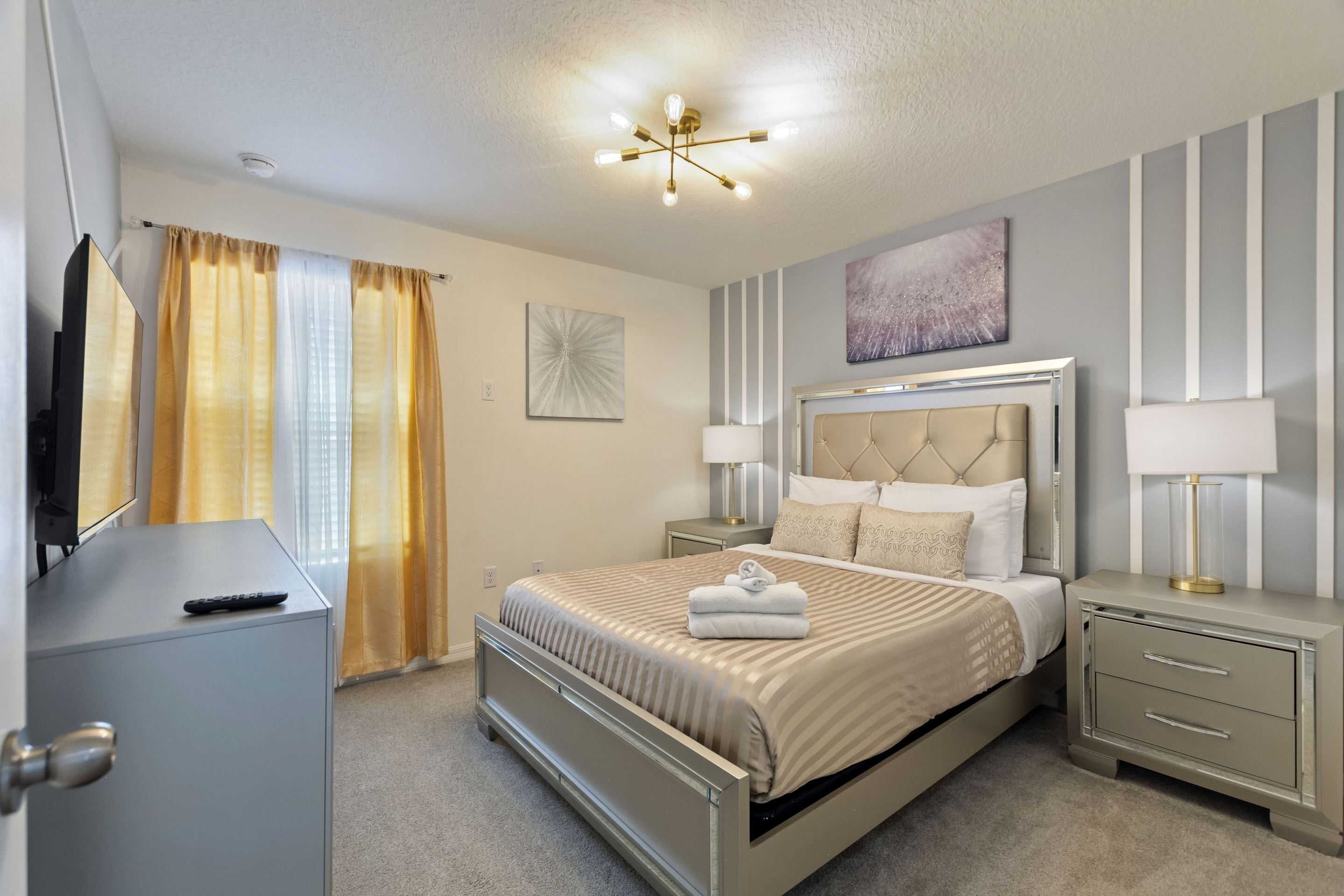 A modern bedroom with a bed, bedside tables, a TV, and a ceiling light fixture.