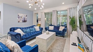 A modern living room with two blue sofas, a marble coffee table, and a large window with curtains. - Rear Views, Spa, Games Room, Pet Friendly, Resort Amenities 8 Bedroom Villa (Kissimmee)
