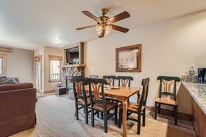 Relax in this open-plan living space with a fireplace, dining area, and large window offering a view of the outdoors.