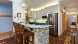 A modern kitchen with granite countertops, stainless steel appliances, and wooden bar stools. - 2708 Chateaux Dmont 3 Bedroom Condo (Keystone)
