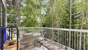 A balcony with a table and chairs, surrounded by a white railing, overlooking a dense forest. - 2708 Chateaux Dmont 3 Bedroom Condo (Keystone)
